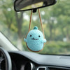 A light blue crocheted animal figure is hanging from a string on a car rearview mirror.