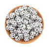 A pile of small white silicone beads with black spotted patterns in a wooden bowl.