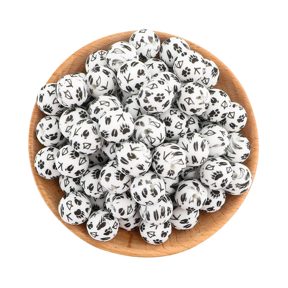 A pile of small white silicone beads with black spotted patterns in a wooden bowl.
