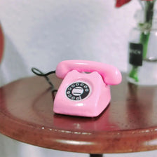 A pink vintage rotary telephone miniature resting on a wooden surface.