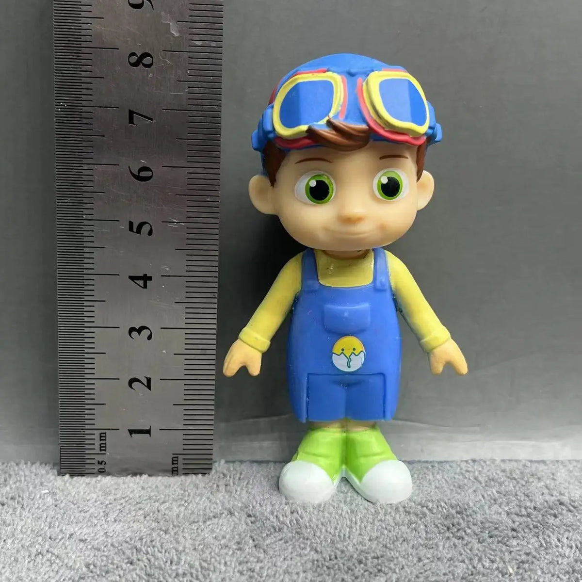 A playful cartoon PVC figurine of a boy dressed in a watermelon school bus design with blue and yellow clothing.