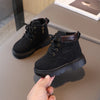 A pair of black kids' winter leather boots with laces and a brown cuff resting on a gray surface.