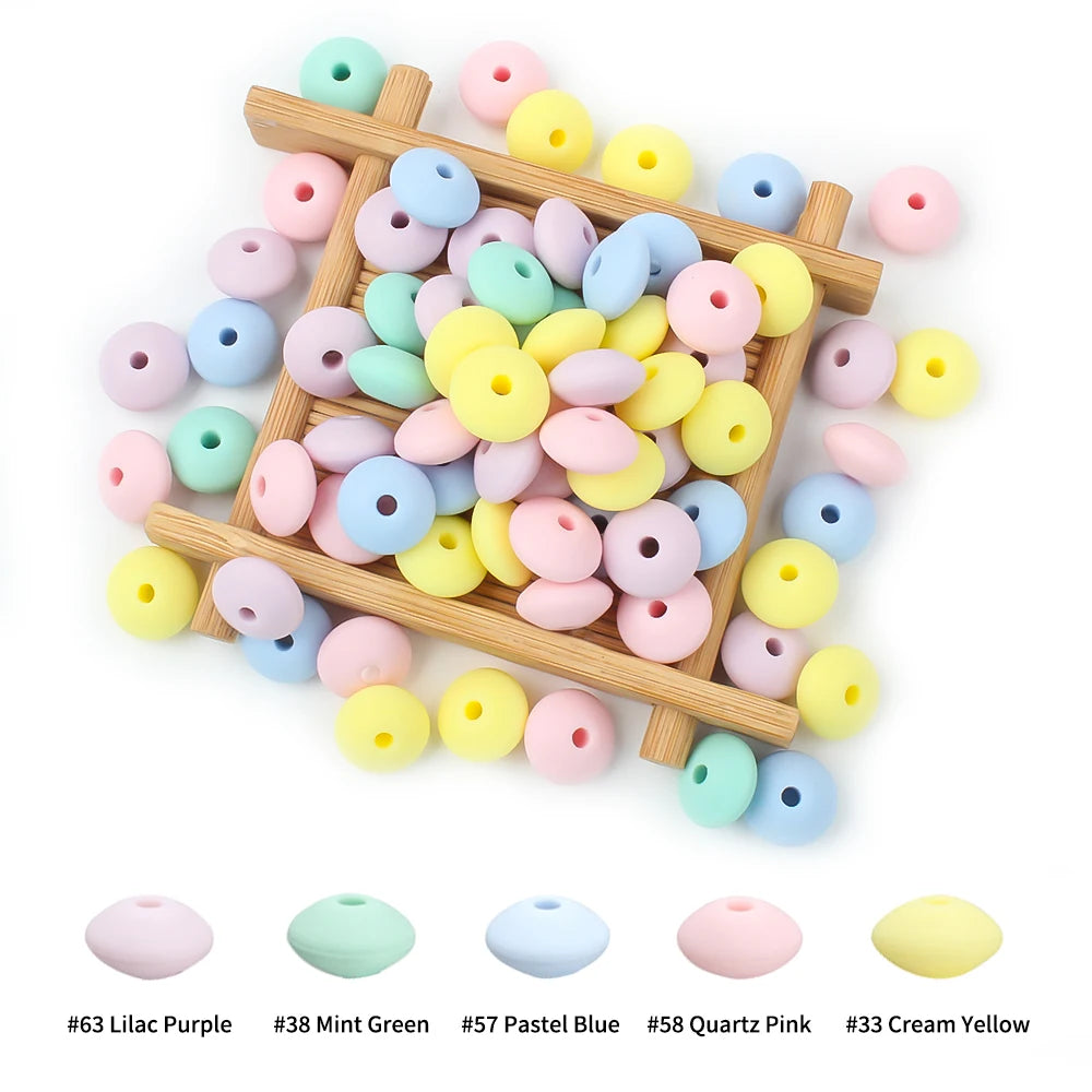 A wooden tray holds various silicone lentil beads in shades of pink, blue, yellow, and green for jewelry making.
