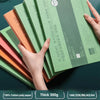 A hand holds a stack of green watercolor paper notebooks with orange and pink covers, showing the thickness and texture.