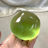 A hand holds a translucent lime green slow rebound squeeze ball, showing a bright glow.