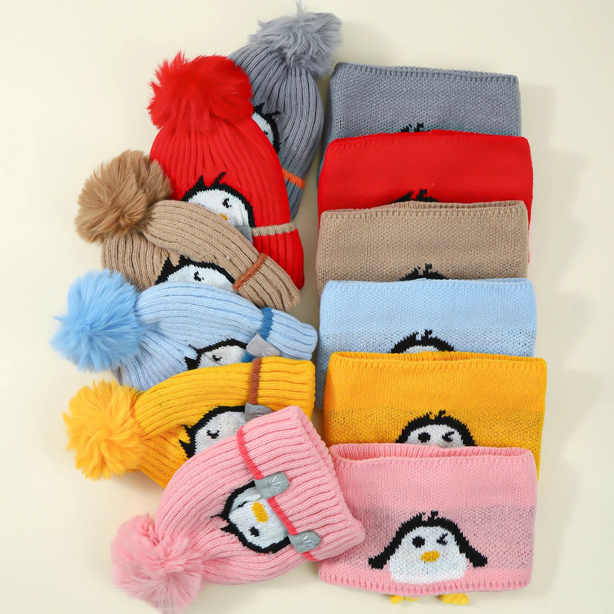 A collection of knitted penguin hats and scarves in various colors including red, gray, blue, yellow, and pink.