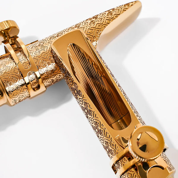 A close-up of a gold-plated tenor saxophone mouthpiece with intricate patterns.
