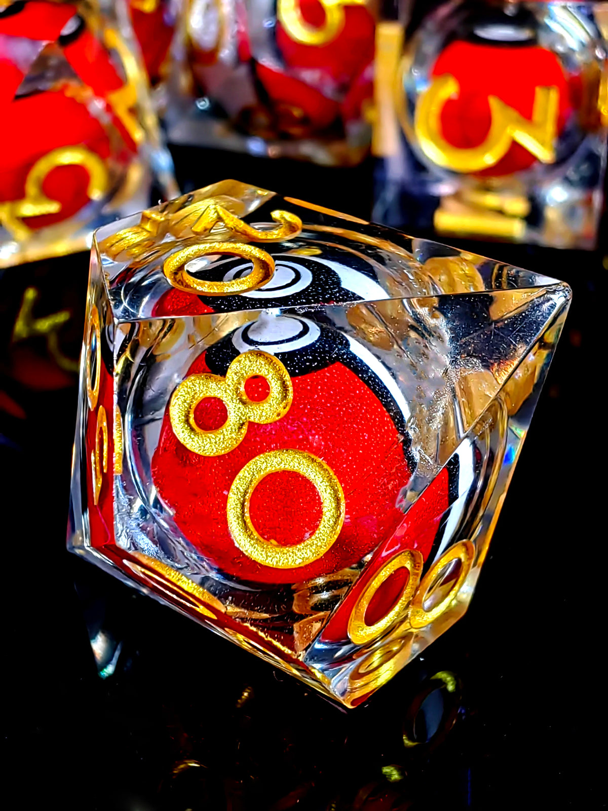 A close-up of a resin die with a red core and gold spinning dragon eye, resting on a reflective black surface.