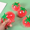 A hand holds a bright red squishy tomato stress relief fidget toy with green leaves against a green background.