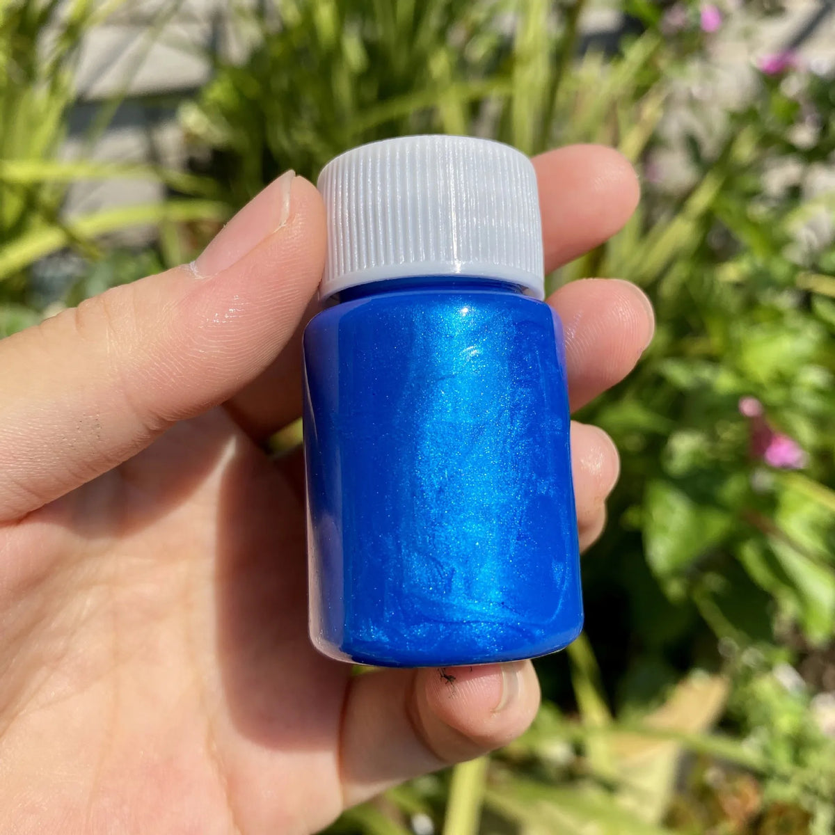 A hand holds a small blue bottle of metallic gold acrylic paint for crafts