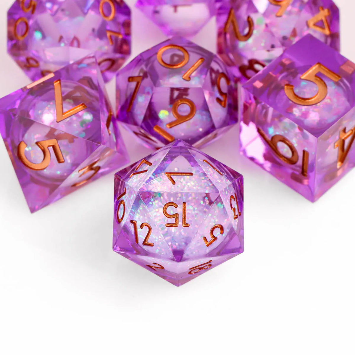 A collection of translucent purple resin dice with gold markings scattered on a white surface.