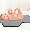 A baby is lying on a gray portable foldable waterproof diaper changing pad on a white bed.