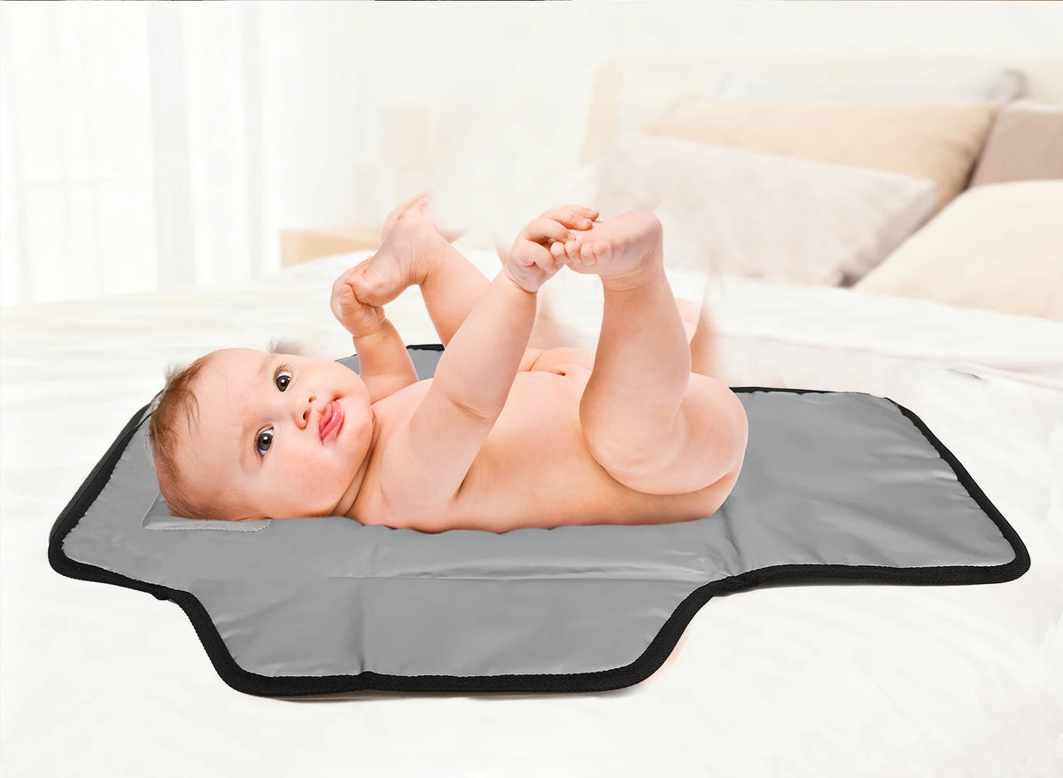 A baby is lying on a gray portable foldable waterproof diaper changing pad on a white bed.
