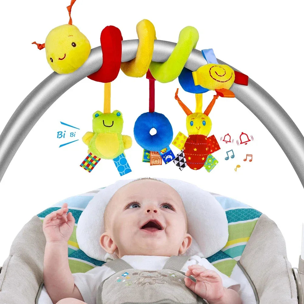 A soft plush hanging baby toy with colorful shapes is shown above a baby in a stroller seat.