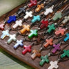 A collection of natural stone cross pendants in various colors and shapes displayed on a wooden board.