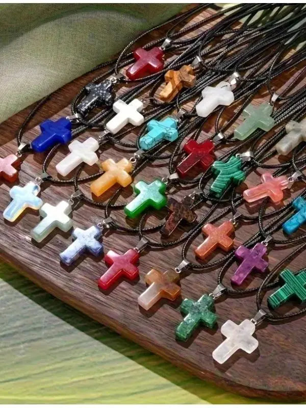A collection of natural stone cross pendants in various colors and shapes displayed on a wooden board.