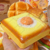 A hand holds a yellow squishy fried egg toast stress relief toy with a cooked orange yolk.