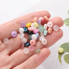 A hand holds a collection of small, round imitation jade glass spacer beads in various pastel and translucent colors.