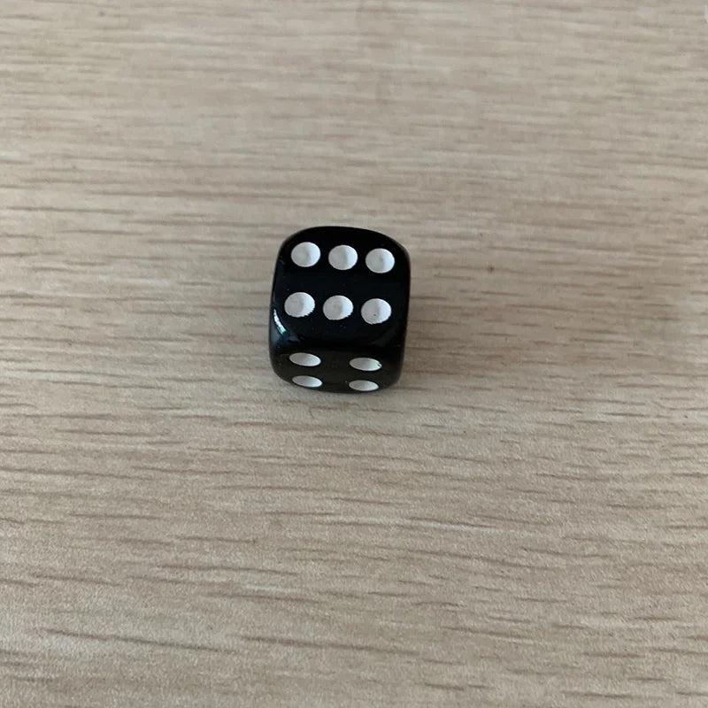 A black die with white dots is placed on a light wooden surface.