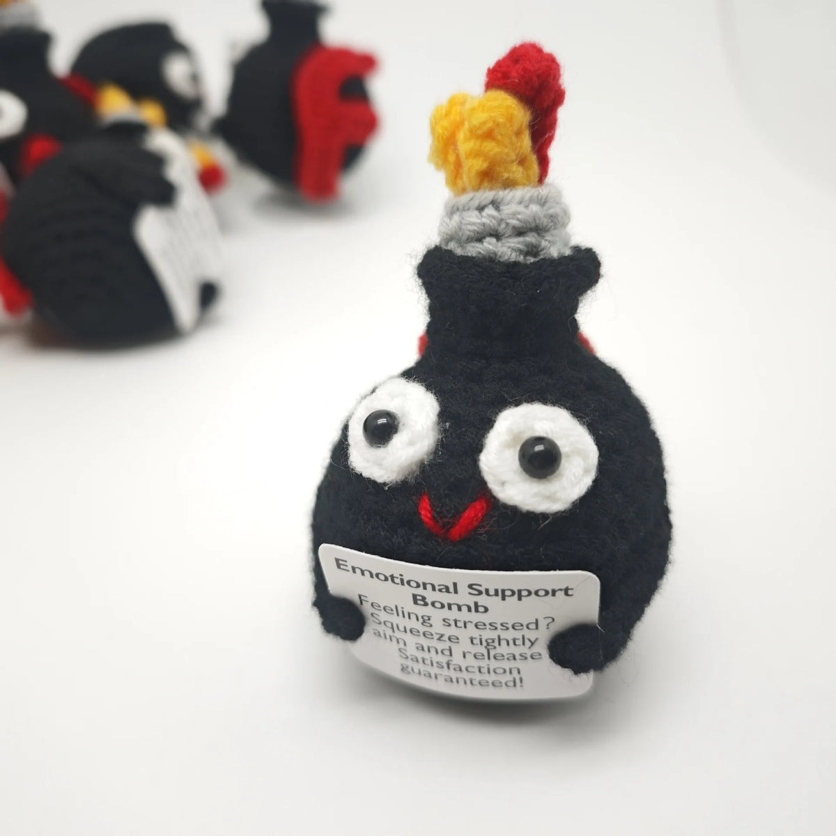 A handmade crochet doll resembling a black bomb with yellow and red accents, featuring an encouragement card.