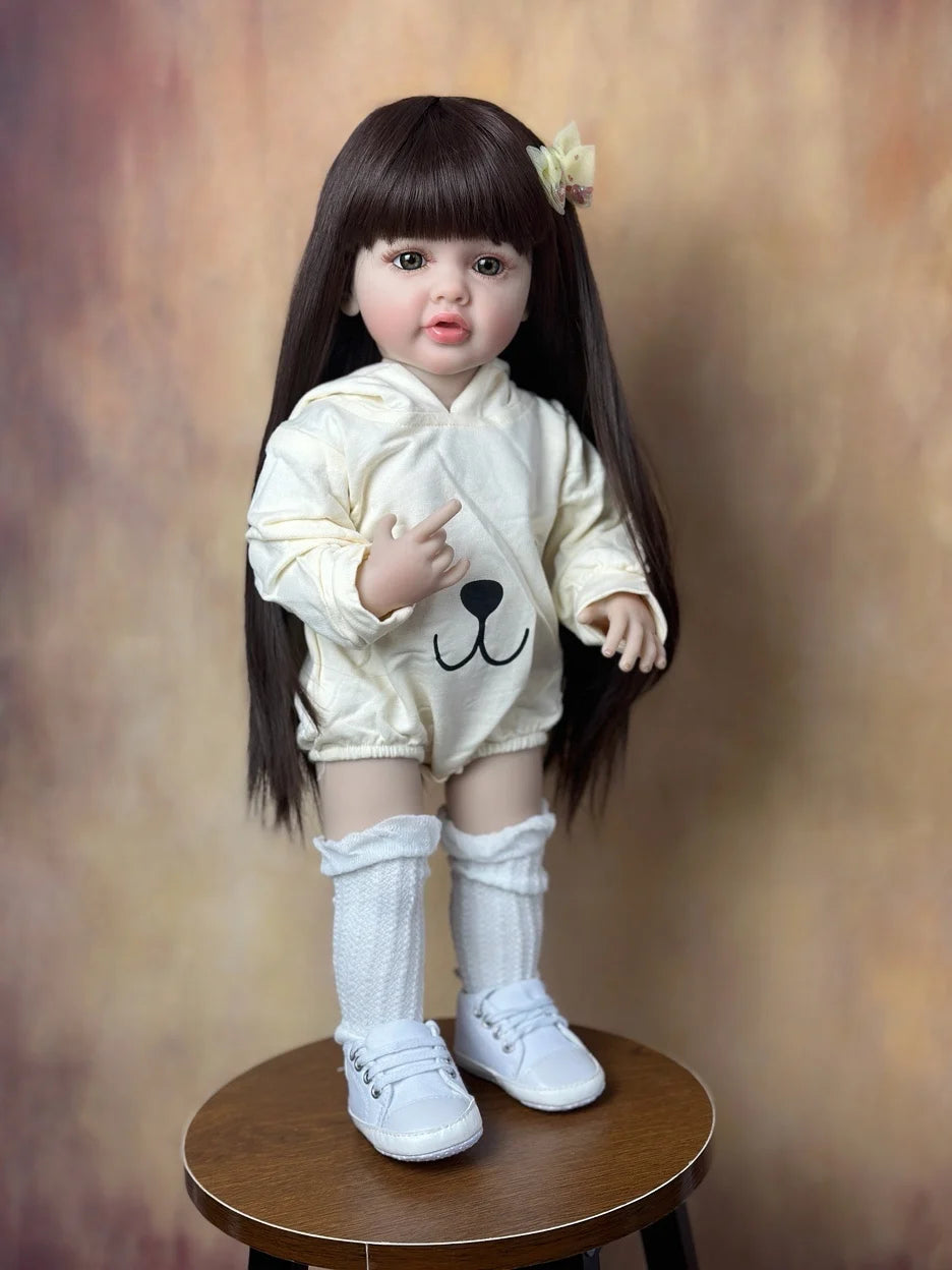 A lifelike 55 cm soft silicone baby doll with long black hair wearing a cream-colored outfit and white socks.