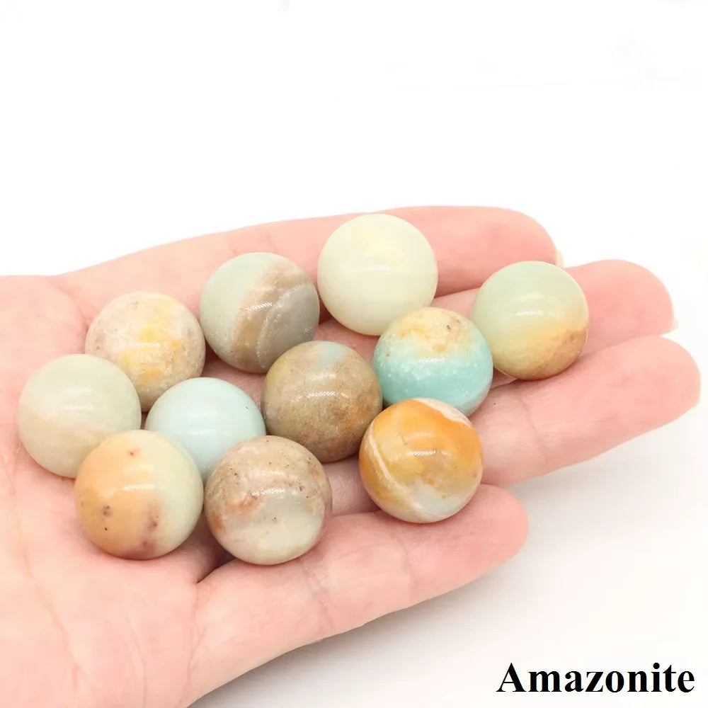 A hand holds several smooth, polished crystal spheres in shades of pink, yellow, and green.
