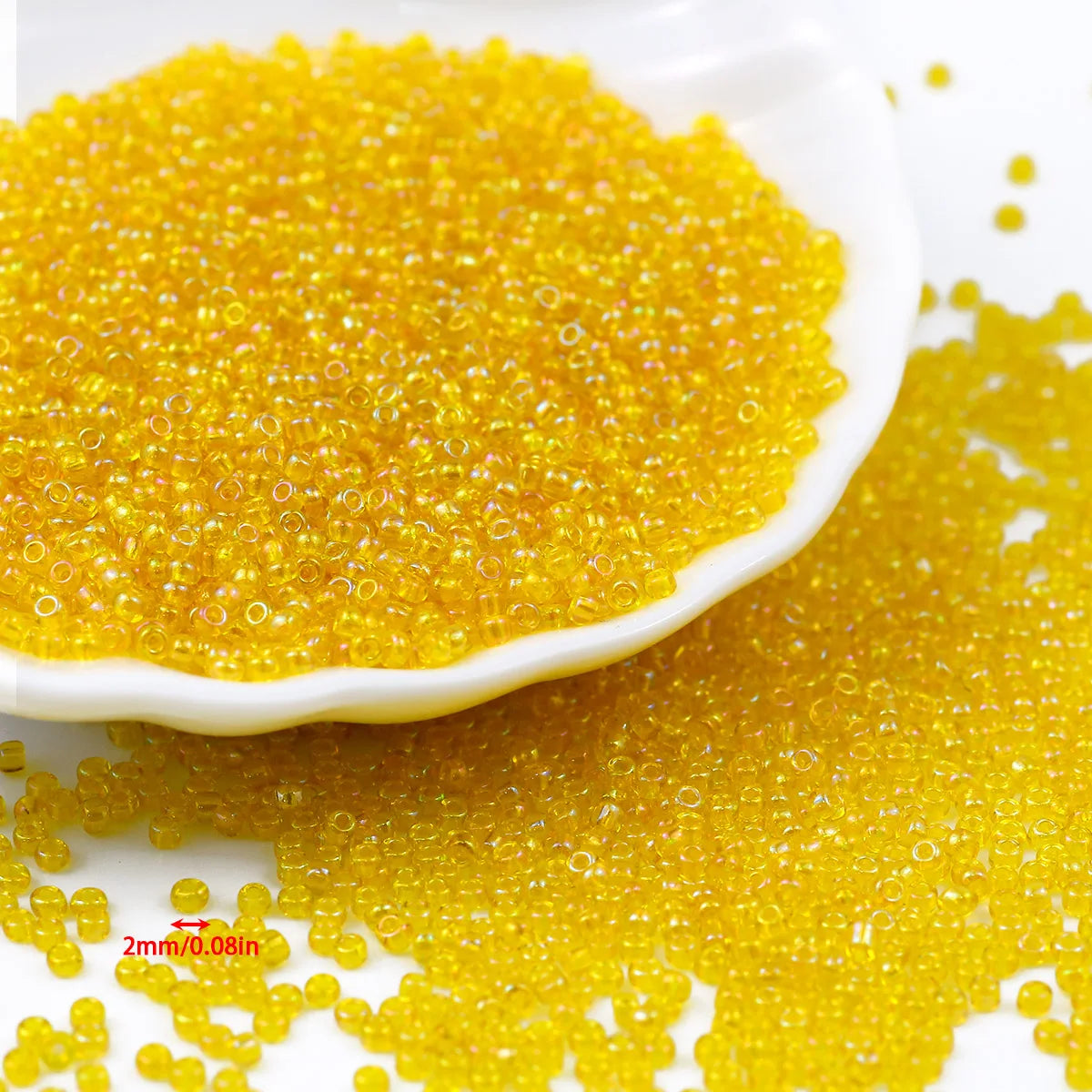 A pile of bright yellow glossy glass seed beads is shown on a white dish and scattered on a surface.