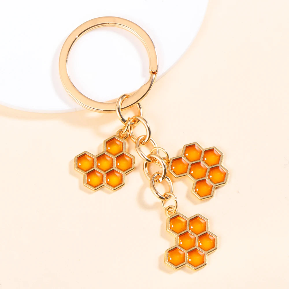 Gold-toned enamel flower keychain with a hexagonal bee design on a white background.