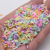 A hand holds a pile of colorful cartoon polymer clay slices in various shapes and colors for slime and craft projects.