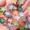 A hand holds a collection of colorful maple leaf glass beads for DIY jewelry making