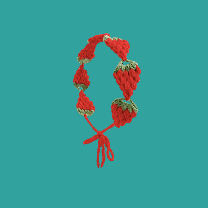 A red strawberry crochet headband with a wide elastic band against a teal background.
