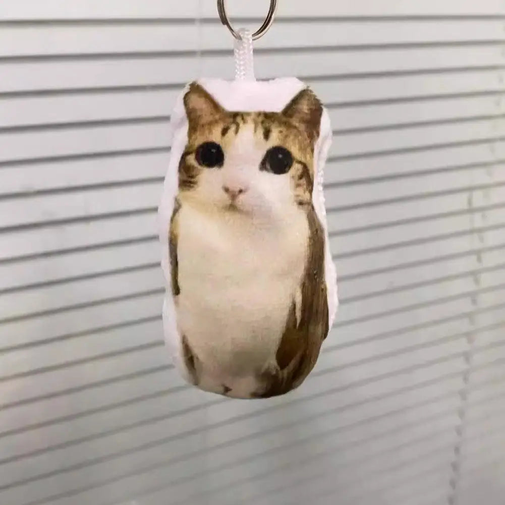 A plush keychain of a cat with brown and white fur is hanging from a silver keyring.