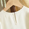 A close-up of a cream long sleeve dress with a bow detail hanging on a wooden hanger.