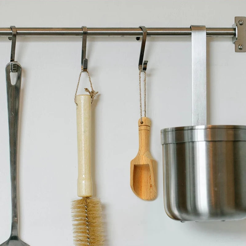 A set of three natural wooden scoop spoons hanging on a metal rack.