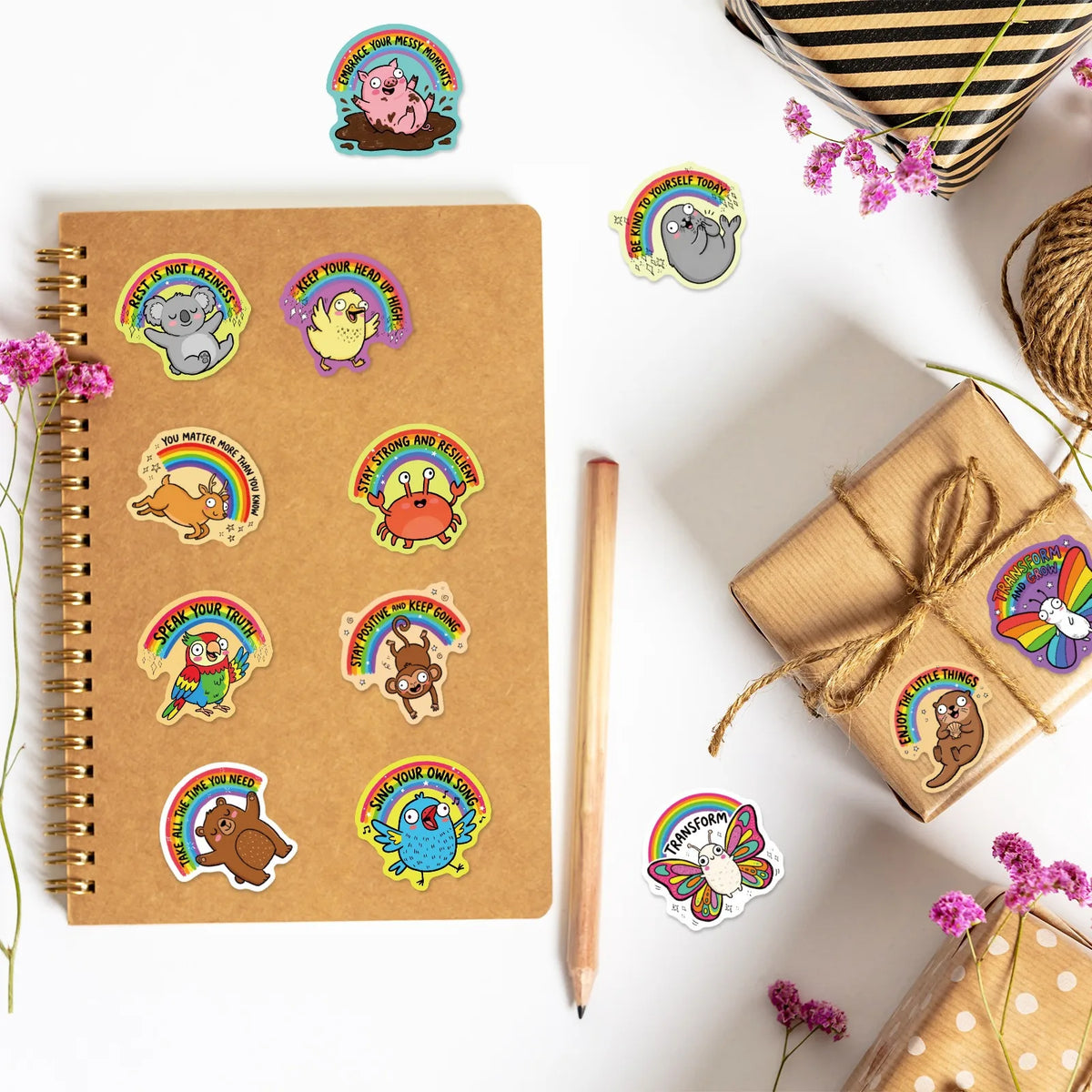 A collection of colorful animal positive quote stickers on a brown spiral notebook and surrounding items.