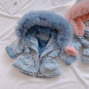 A light blue denim jacket with a fluffy blue faux fur collar and pink lining is displayed on a white surface.