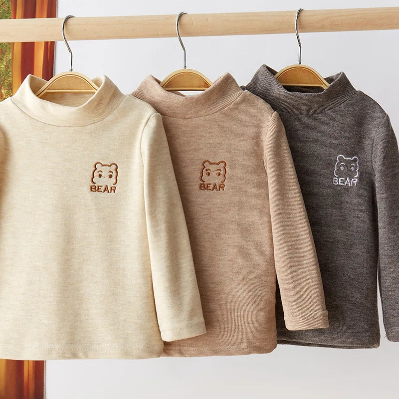 A beige long sleeve shirt with a bear embroidery hanging on a wooden hanger.