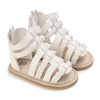 A pair of cream-colored baby first walker sandals with braided straps and a soft anti-slip sole.