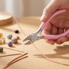 A hand holds pink jewelry pliers, preparing to work on thin copper wire for making jewelry.