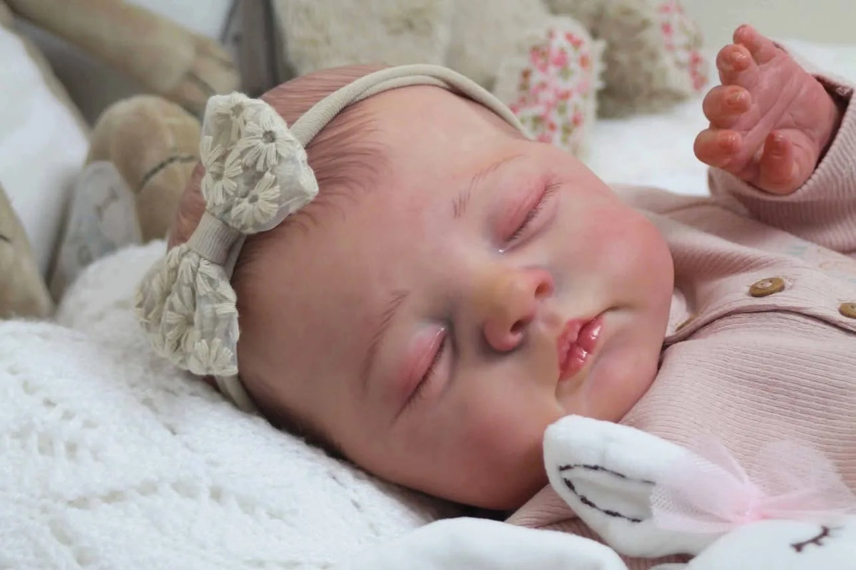 A newborn reborn baby doll with soft cloth body is sleeping peacefully on a white blanket.