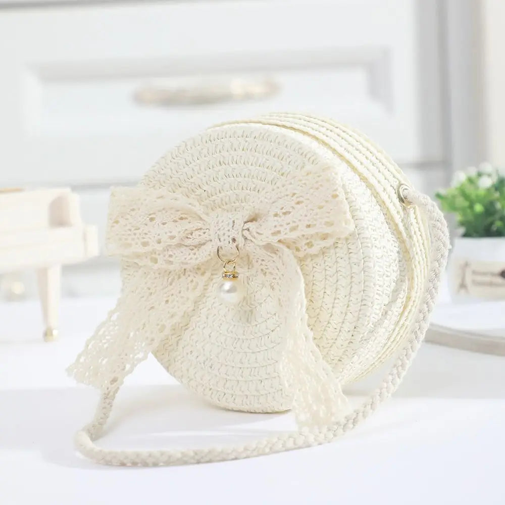A white handwoven straw crossbody bag featuring a delicate lace bow detail.