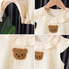 A set of cream-colored cotton muslin baby romper and hat featuring a brown bear applique.