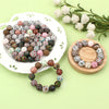 A collection of colorful printed silicone beads in various patterns is displayed on a white plate and a wooden ring.