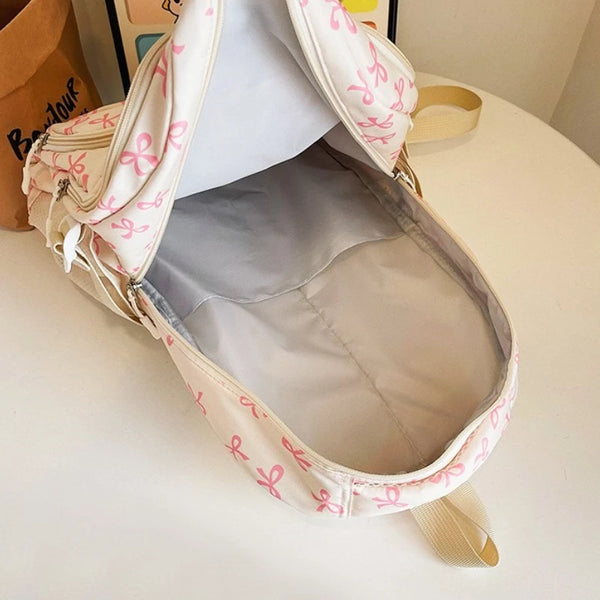 Ein hellrosa Rucksack mit weißer Schleifenmuster, geöffnet, zeigt das Innenfutter.