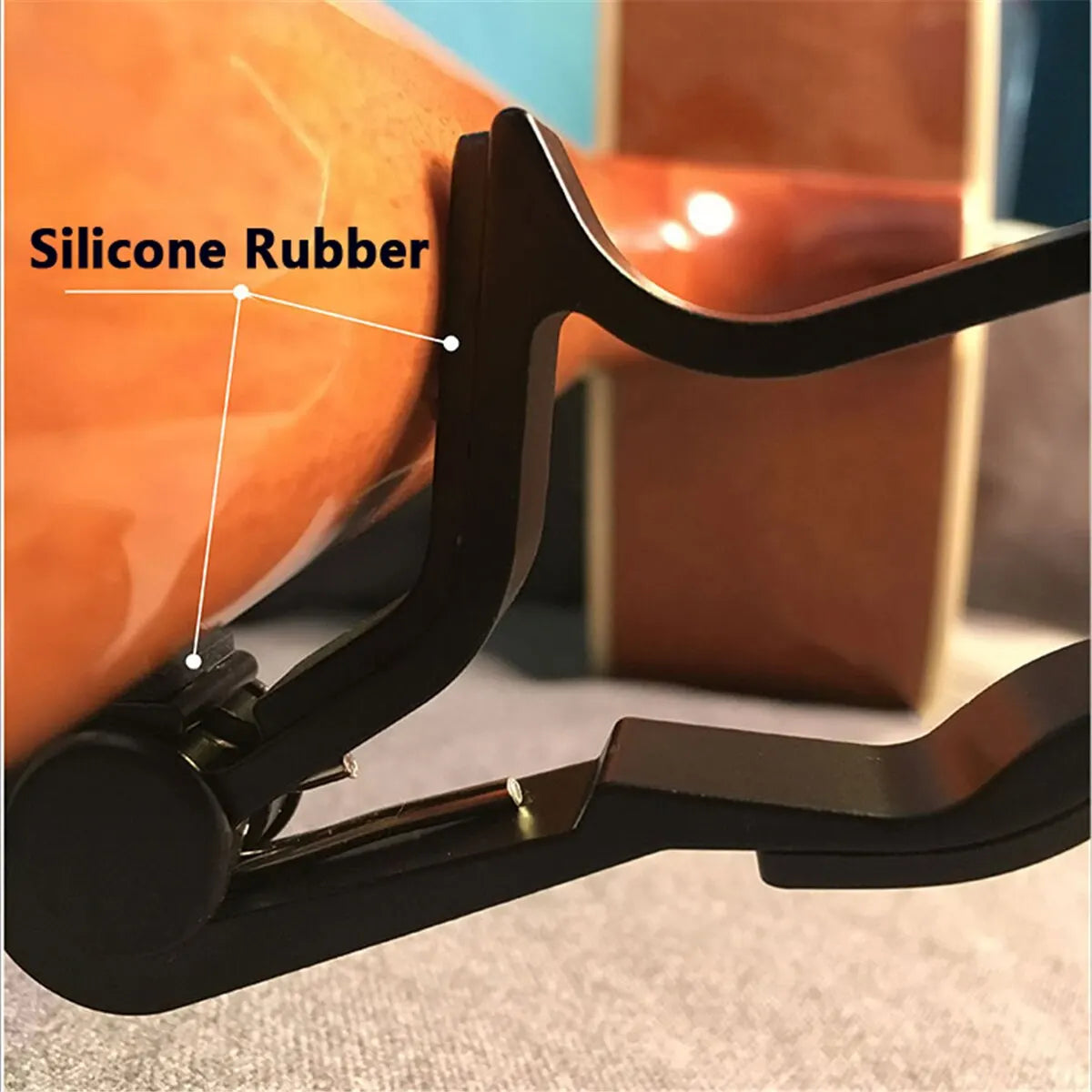 Gros plan sur une pièce en silicone noir, utilisée comme accordeur réglable pour guitare acoustique et électrique.