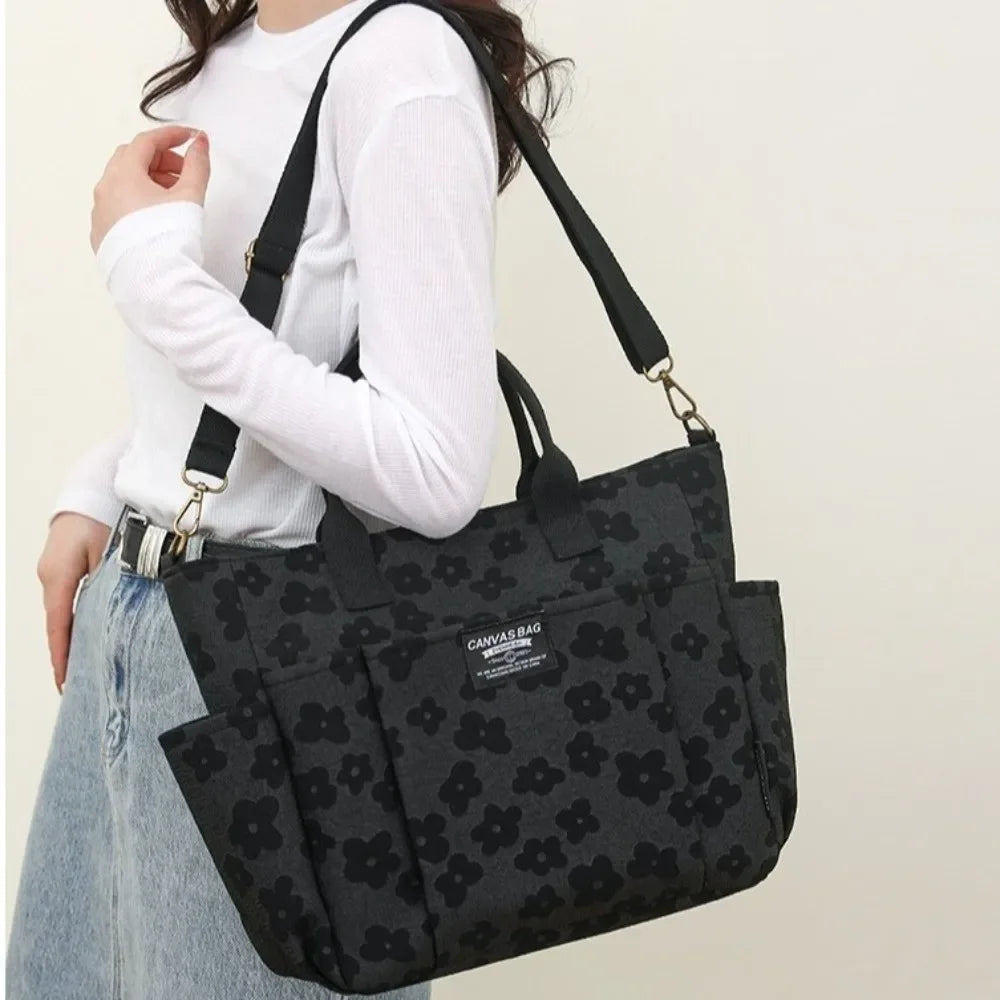 A woman holds a black canvas tote bag with floral pattern and multiple pockets against a light background.