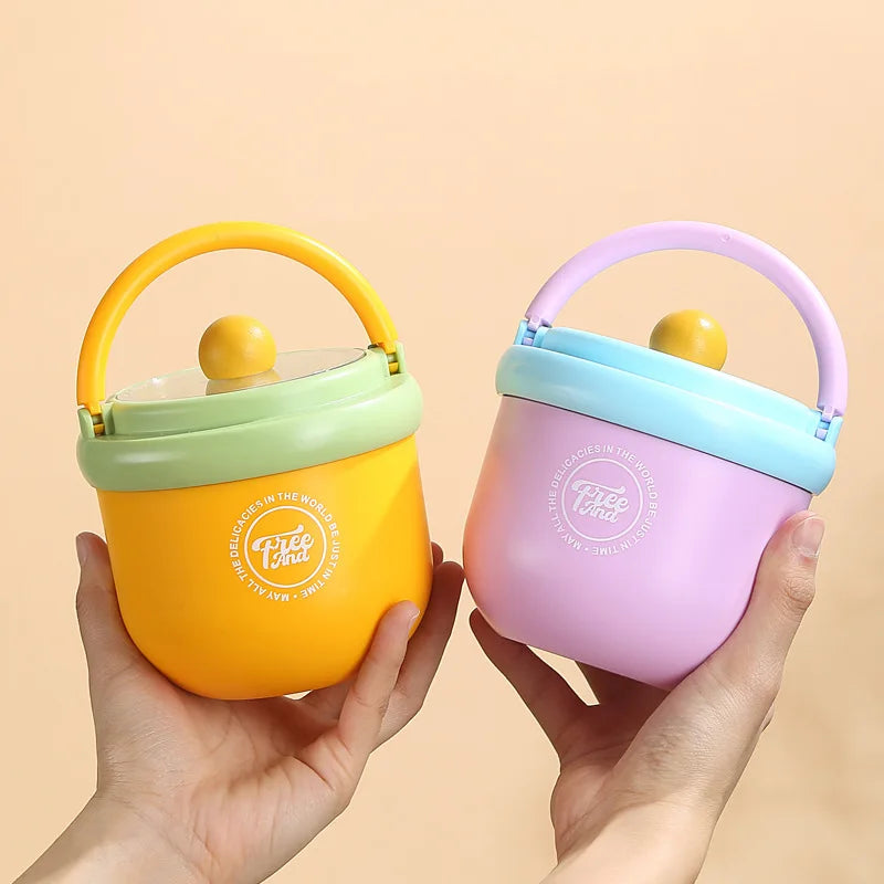 A hand holds a pink insulated stainless steel breakfast cup with a lid and a yellow silicone handle against a light backgroun
