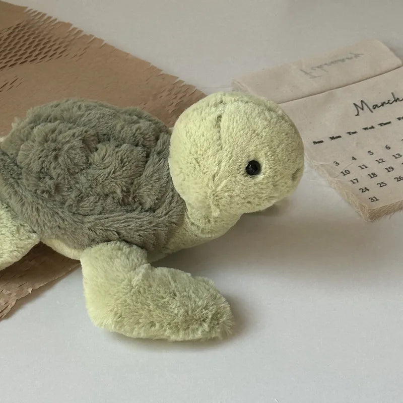 A soft, light green simulated turtle plush doll lying on a white surface next to a calendar.