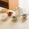 A wooden pretend play tea party set featuring various cups and a teapot arranged on a light wooden table.