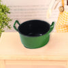 A small, dark green miniature copper soup pot sitting on a light wooden surface.